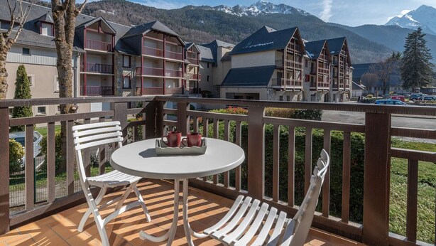Un balcon avec une table et des chaises, offrant une vue sur un paysage montagneux et les bâtiments de l’hôtel.