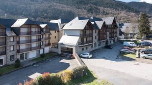 Une rangée de bâtiments de style chalet traditionnel, dotés de balcons, un espace de stationnement et un paysage montagneux en arrière-plan.