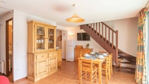 Una sala de estar acogedora con comedor, muebles de madera, una escalera y una cocina al fondo.