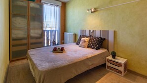 Une chambre à coucher comprenant un lit, une table de chevet, un radiateur, une fenêtre avec des rideaux et une porte-fenêtre coulissante.