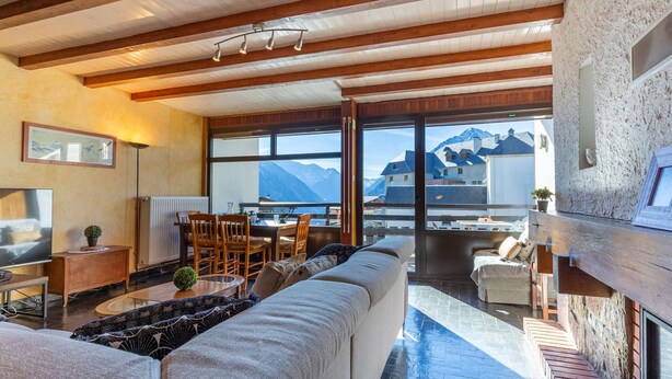Un vaste espace de vie comprenant un grand canapé, une table à manger avec des chaises et une vue sur les montagnes grâce à de grandes fenêtres.