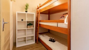 Un lit superposé avec une étagère blanche à côté, sur laquelle se trouvent une plante en pot et une petite boîte.