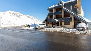 Un immeuble à plusieurs étages, doté d’un toit en pente, avec un télésiège et une montagne enneigée en arrière-plan.