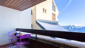 Un balcon avec une chaise et une table violettes, un toit recouvert de neige et une vue sur les montagnes.