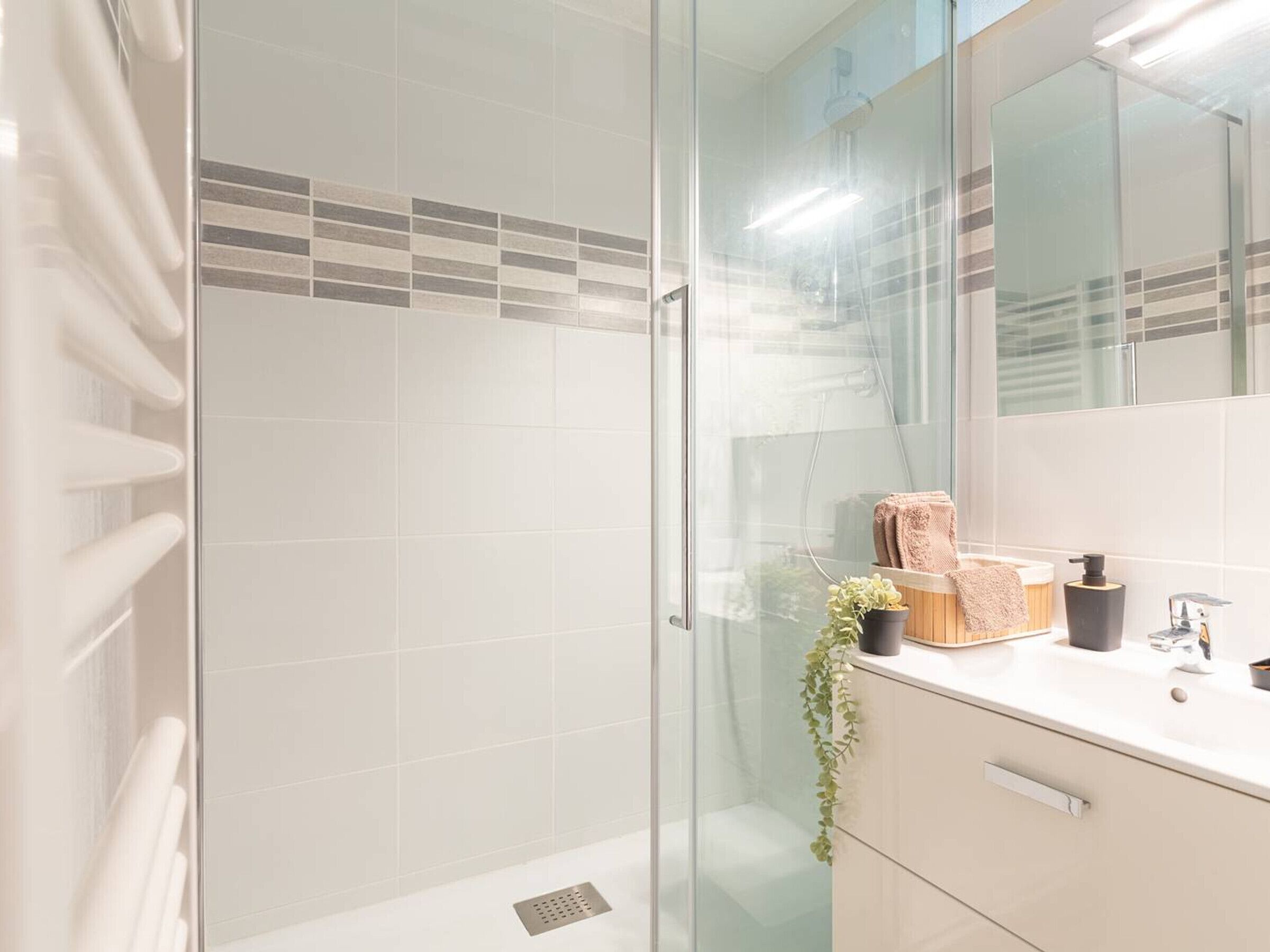 Een moderne badkamer met een douchecabine van glas, een witte wastafel met spiegel en een kamerplant.