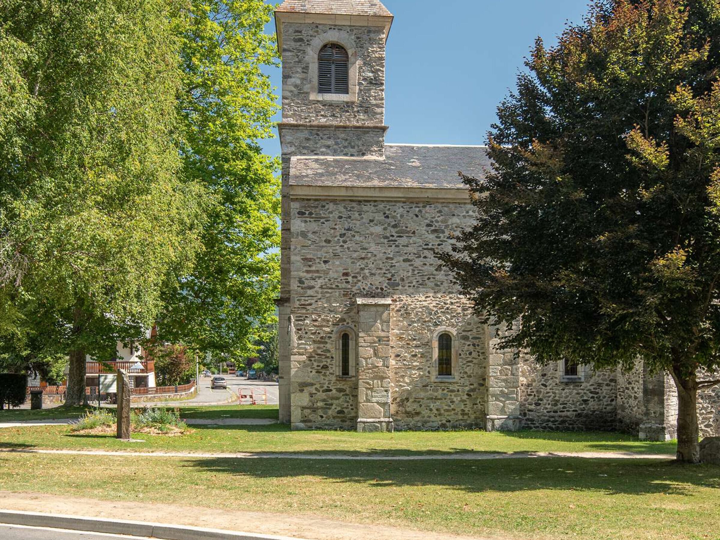 A stone church with a bell tower, surrounded by trees and a grassy area.