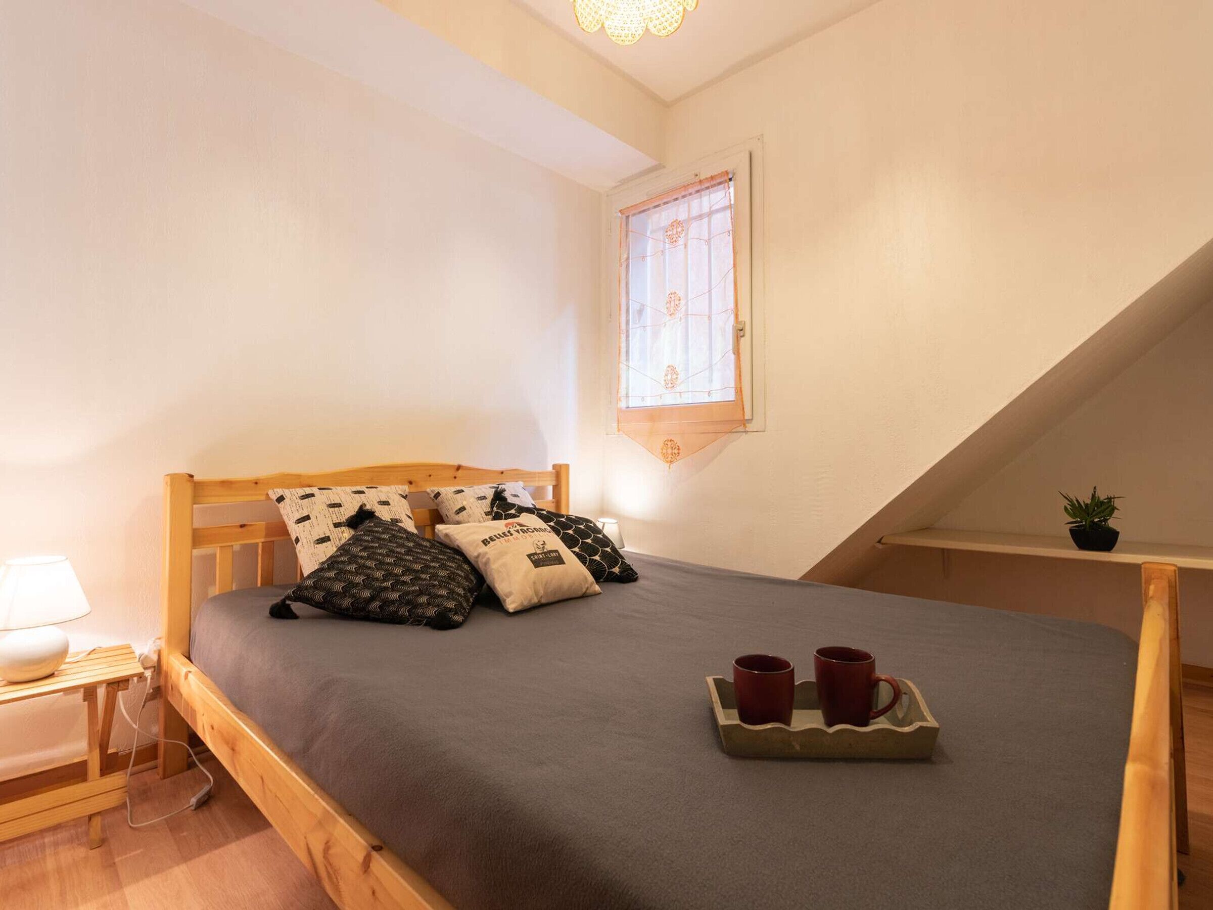 A small, cozy bedroom with a single bed, a bedside table with a lamp, and a window with a curtain.
