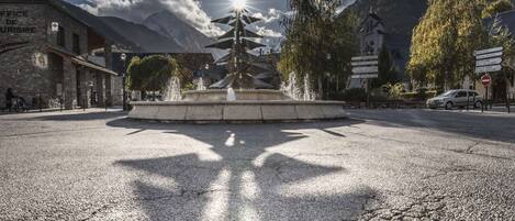Una plaza con una fuente, rodeada de edificios y montañas.