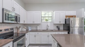 Una cocina moderna con armarios blancos, electrodomésticos de acero inoxidable, una ventana con planta y una cafetera.