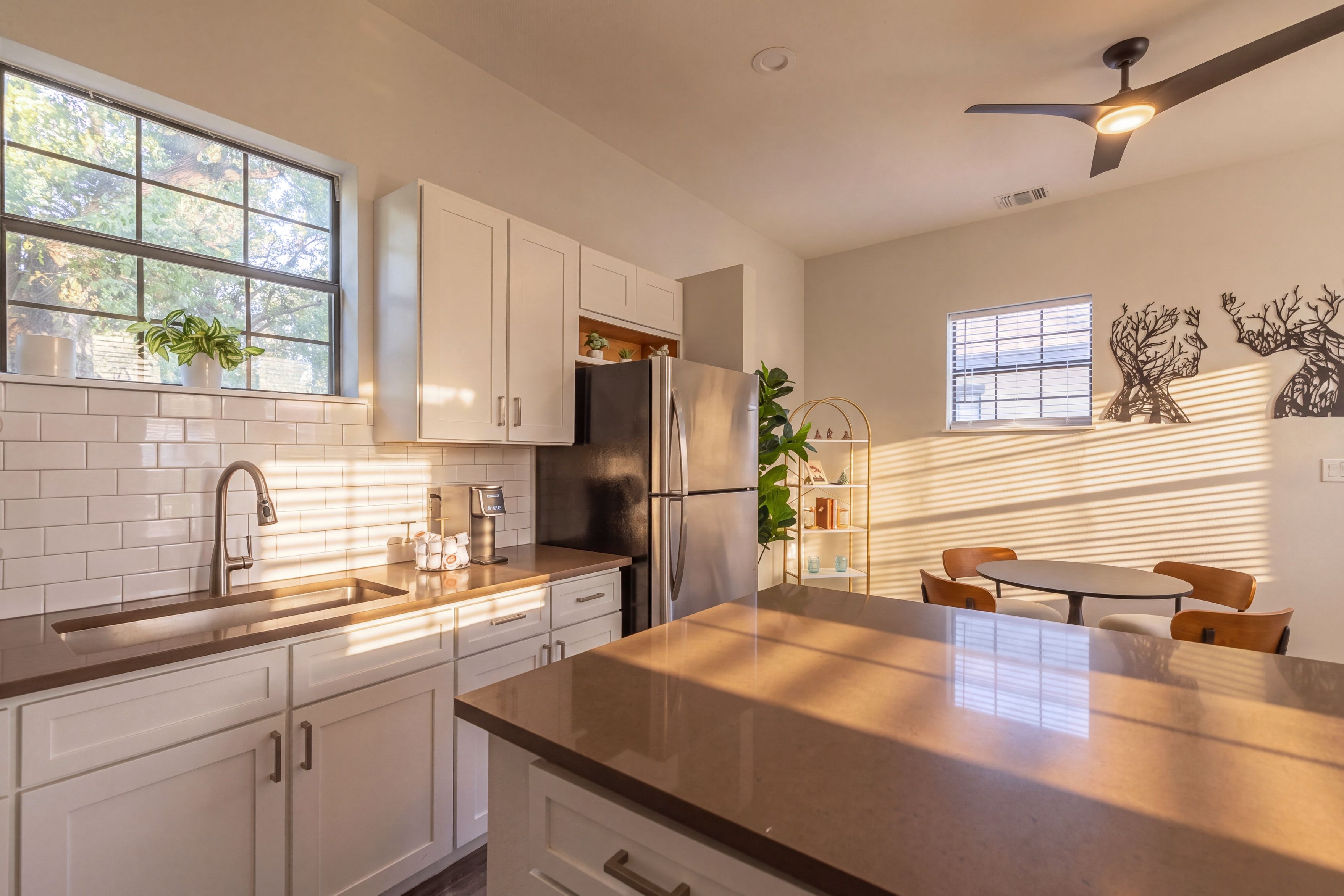 A modern kitchen with white cabinets, a stainless steel refrigerator, and a dining area with a table and chairs.