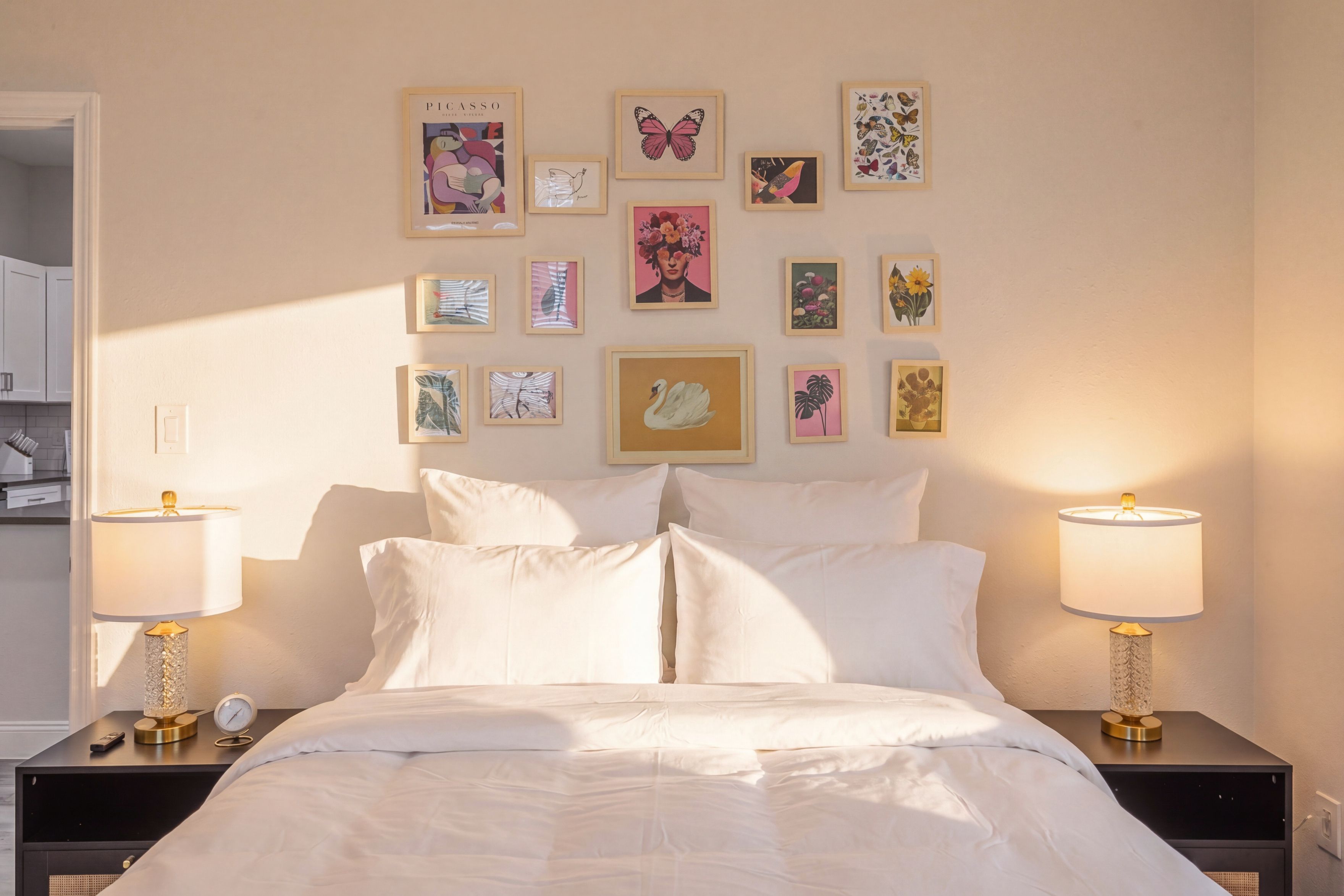 A hotel room with a bed, two bedside lamps, and a wall decorated with various framed artworks.