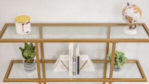 Una estantería metálica con tapa de vidrio, una vela blanca, un pequeño globo terráqueo y dos macetas con plantas.