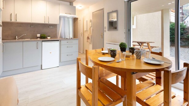 Eine moderne Küche mit weißen Schränken, einem eingebauten Backofen und einem Essbereich mit Holztisch und Stühlen.