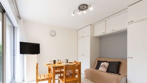 Ein moderner, gut beleuchteter Raum mit Esstisch und Stühlen, einer Couch und einem an der Wand befestigten Fernseher.