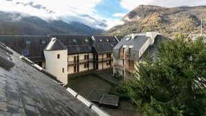 A traditional chalet-style building with multiple dormer windows, a courtyard, and a mountainous backdrop.