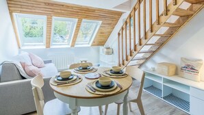A dining area with a round table set for four, a wooden staircase, and a view of greenery outside.