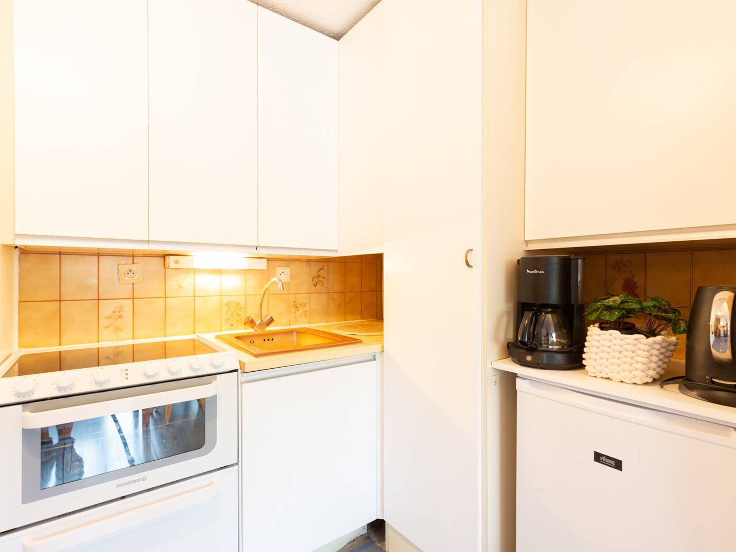 A compact kitchen with white cabinets, a built-in oven, a sink, and a coffee maker.