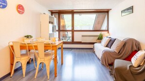 A cozy room with a wooden dining table and chairs, a sofa, and a window with a view of greenery. - Apartment for 4 in Saint-Lary-Soulan, near center and cable car (Saint-Lary-Soulan)
