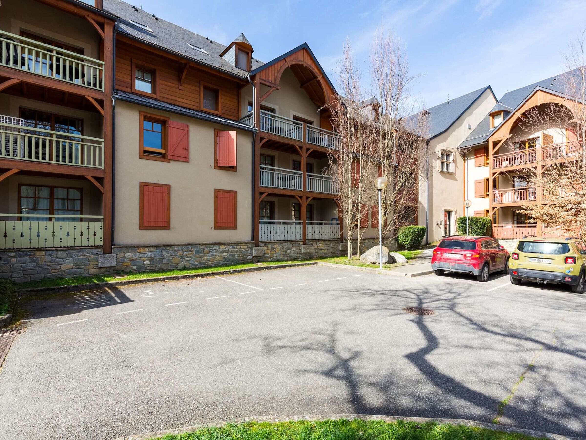 Un edificio de varios pisos con balcones, fachada de piedra y un estacionamiento con coches.