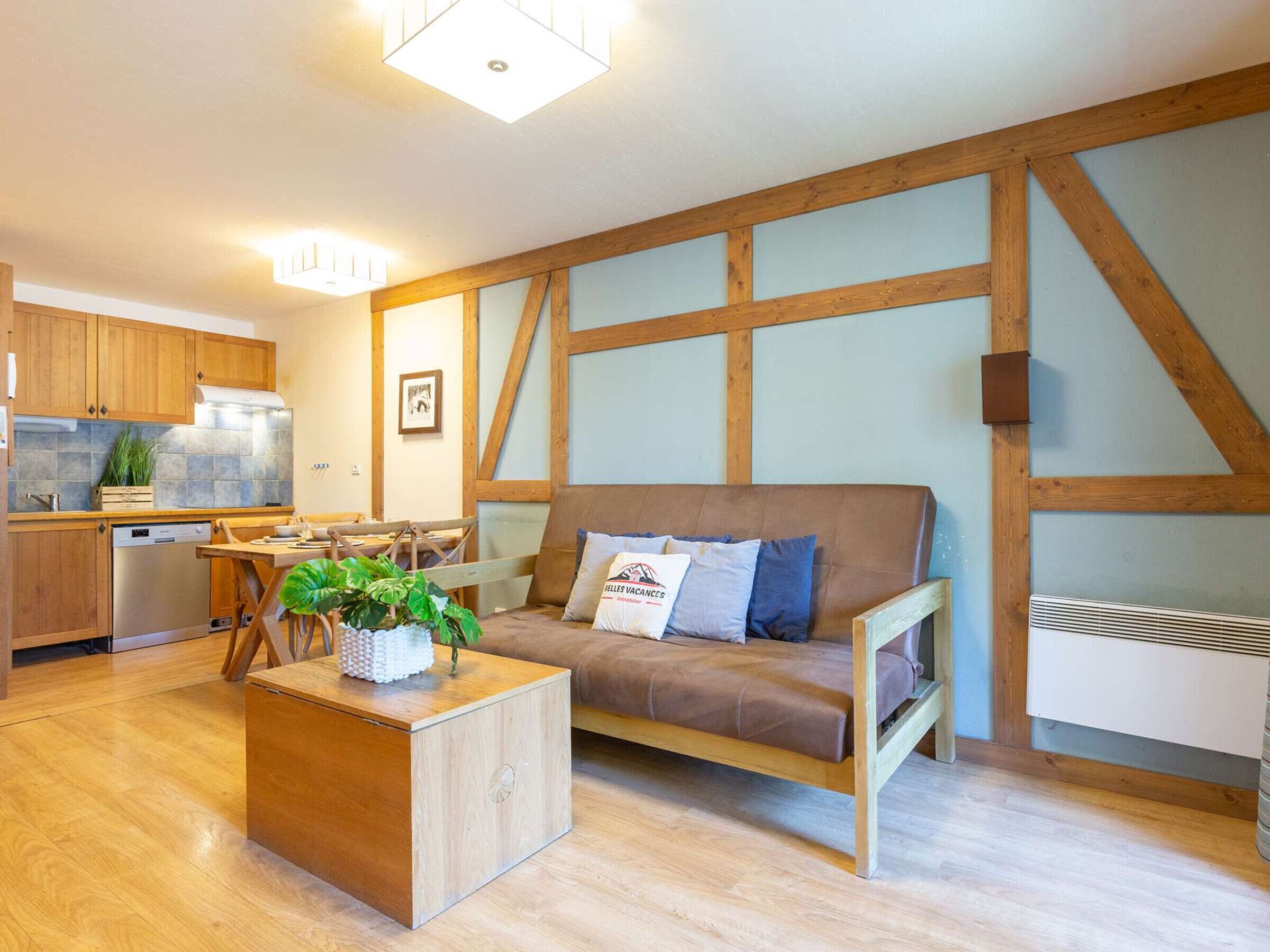 Ein gemütlicher Wohnbereich mit einer Holzsofa, einem kleinen Holztisch mit Pflanze und einer Küche im Hintergrund.