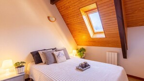A cozy bedroom with a sloped ceiling, a skylight, a bed with pillows, a bedside table with a lamp, and a small plant.