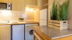 A compact kitchen with wooden cabinets, a microwave, a dishwasher, a washing machine, and a countertop with a potted plant.