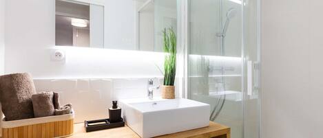 A modern bathroom with a white sink, a mirror, a glass shower enclosure, and a wooden vanity.