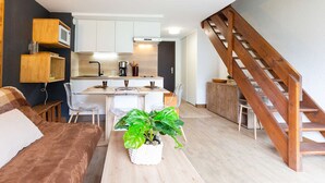 Un espacio habitable compacto con kitchenette, comedor y una escalera.