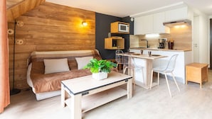 Un espacio habitable compacto con una pared de acento de madera, una kitchenette, un sofá, una mesa de comedor y una planta en maceta.