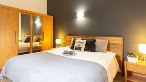 Un dormitorio con cama, armario de madera, lámparas de noche y una mesita con una planta.