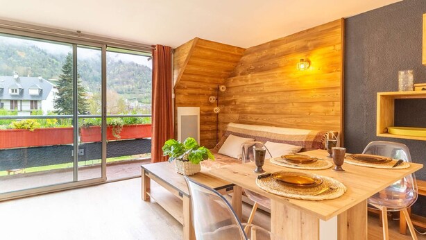 Un comedor moderno con una mesa de madera dispuesta para cuatro personas, un banco y vistas a un paisaje montañoso a través de amplios ventanales.