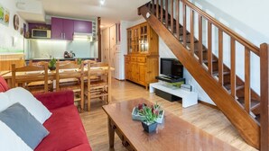 Una sala de estar moderna con una escalera de madera, un comedor con muebles de madera y una cocina con armarios morados.