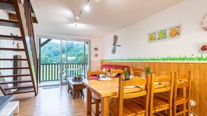 Un comedor con mesa y sillas de madera, un banco acolchado rojo y vistas a zonas verdes a través de un ventanal corredero.
