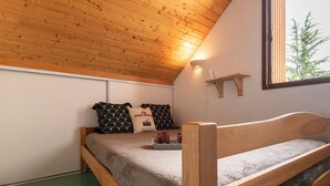 A wooden bunk bed with a grey blanket, two patterned pillows, a small shelf, and a window with a view of trees. - Quiet apartment, 8 people, near center, parking, Saint Lary Soulan (Saint-Lary-Soulan)