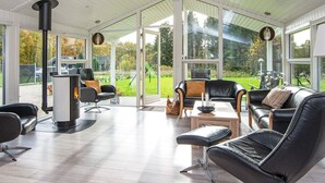 A modern living room with a wood-burning stove, leather furniture, and large windows offering a view of the garden. - Luxury Spa Retreat in Arrild - By Traum Ferienwohnungen (Toftlund)