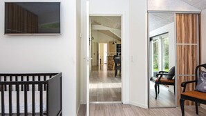 A modern interior with a wooden floor, a black crib, a dining area with chairs, and a kitchen visible through an open door. - Luxury Spa Retreat in Arrild - By Traum Ferienwohnungen (Toftlund)