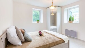 A bedroom with a bed, two windows, a radiator, and a hanging light fixture.