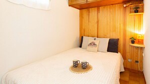 A cozy room with a bed, wooden paneling, a small table with a lamp, and a sign indicating it's a vacation rental. - Quiet Apartment near Saint-Lary Center, 700m from Cable Car, Max 5 People (Saint-Lary-Soulan)