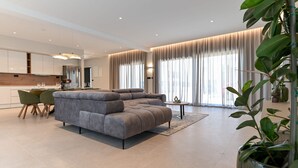 A modern living room with a grey sectional sofa, a dining area with a small table and chairs, and large windows with curtains. - Villa Azzurra Zadarvillas (Sukosan)