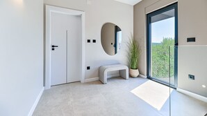 A modern hallway with a white door, a bench, a potted plant, and a large window offering a view of greenery. - Villa Azzurra Zadarvillas (Sukosan)