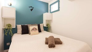 A neatly made bed with a white duvet and two brown towels, a teal accent wall, a small window, and a wall-mounted shelf with a plant. - Quiet apartment Saint Lary, 4 people, near center, wifi included (Saint-Lary-Soulan)