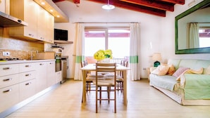 Een moderne keuken met houten kastjes, een eettafel met stoelen, een bank en een groot raam met gordijnen.