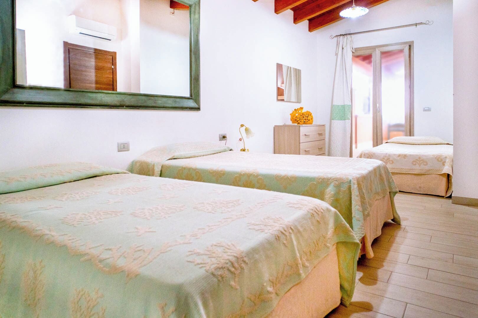 Une chambre avec deux lits, un miroir, une commode, une lampe et une fenêtre avec des rideaux.