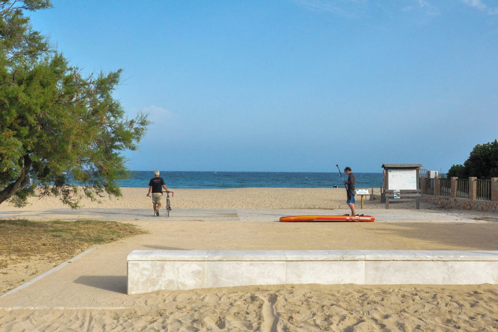 Una playa con un paseo de hormigón, un cartel y una caseta de socorristas.
