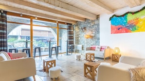 A spacious living area with a stone wall, a colorful abstract painting, and a view through large windows. - Apartment in Saint-Lary-Soulan with Pool & Sauna - 6 ppl (Saint-Lary-Soulan)
