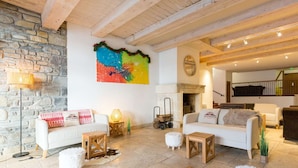 A spacious living area with a stone wall, a colorful abstract painting, a fireplace, and a wooden ceiling. - Apartment in Saint-Lary-Soulan with Pool & Sauna - 6 ppl (Saint-Lary-Soulan)