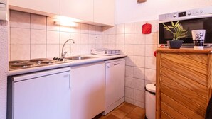 Una cocina compacta con muebles blancos, un lavamanos de acero inoxidable, un microondas y un pequeño armario de madera.