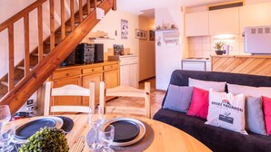 Una sala de estar acogedora con una escalera de madera, un comedor con una mesa dispuesta para dos personas y una cocina equipada con refrigerador y microondas.