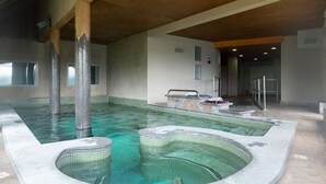 An indoor swimming pool with a tiled floor, a hot tub, and a changing area.
