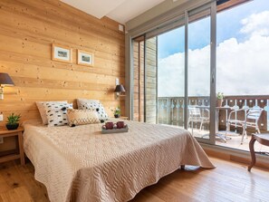 A bedroom with a large bed, wooden walls, and a balcony with outdoor furniture. - Ski-in/Ski-out apartment with heated pool and parking (Saint-Lary-Soulan)